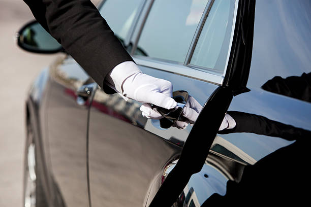 Professional airport taxi driver opening the car door for a passenger before an airport transfer.